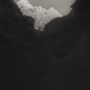 A dry creek bed leads the viewer into a small side canyon to the Colorado River in Grand Canyon National Park with the tops of the canyon walls lit by the early morning sun while the rest of the canyon is in shadow.