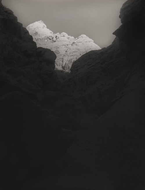 A dry creek bed leads the viewer into a small side canyon to the Colorado River in Grand Canyon National Park with the tops of the canyon walls lit by the early morning sun while the rest of the canyon is in shadow.